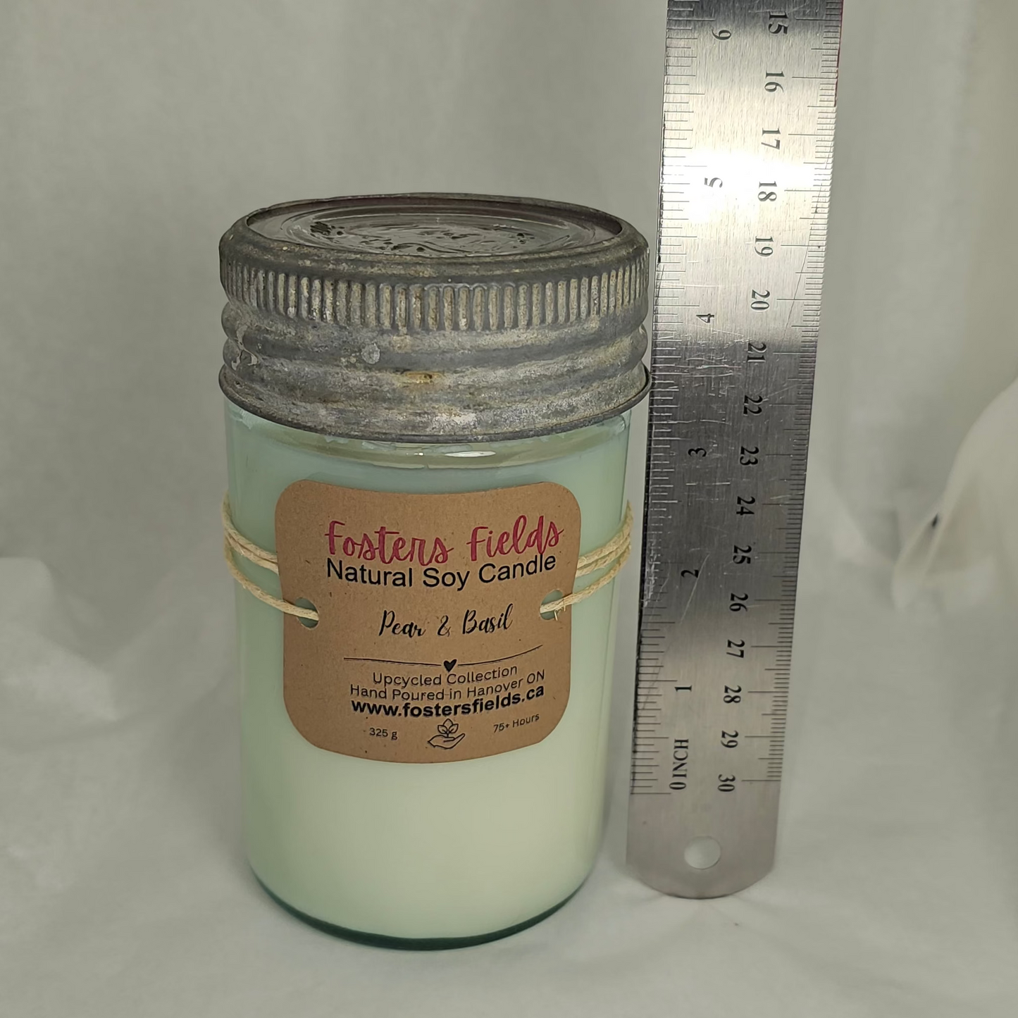 Candle jar with a label and ruler for scale on a white background