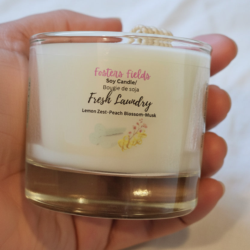 Hand holding a candle labeled 'Fresh Laundry' with visible branding.