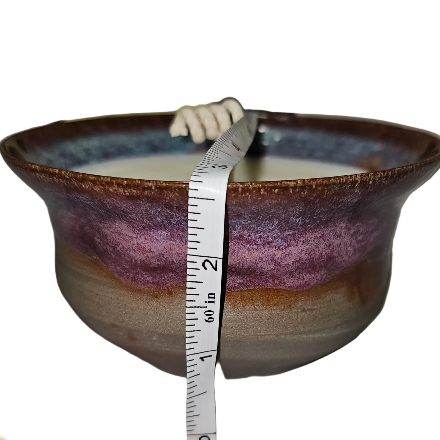 Ceramic bowl with a hand holding a measuring tape against it, on a white surface. soy candle
