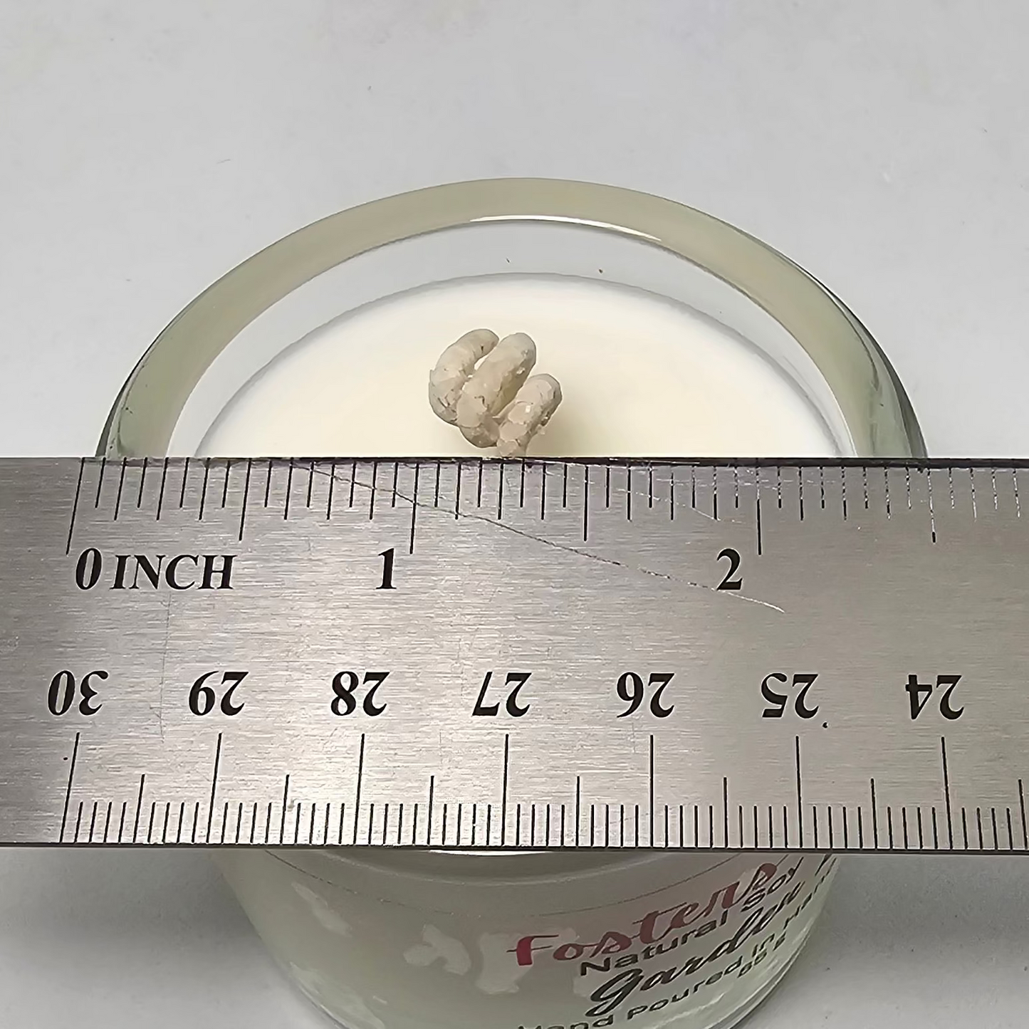Clear glass container with a white soy wax poured into it, measured against a metal ruler on a white background.