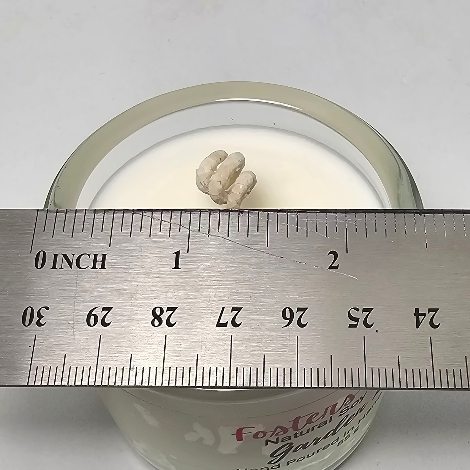 Clear glass container with a white soy wax poured into it, measured against a metal ruler on a white background.