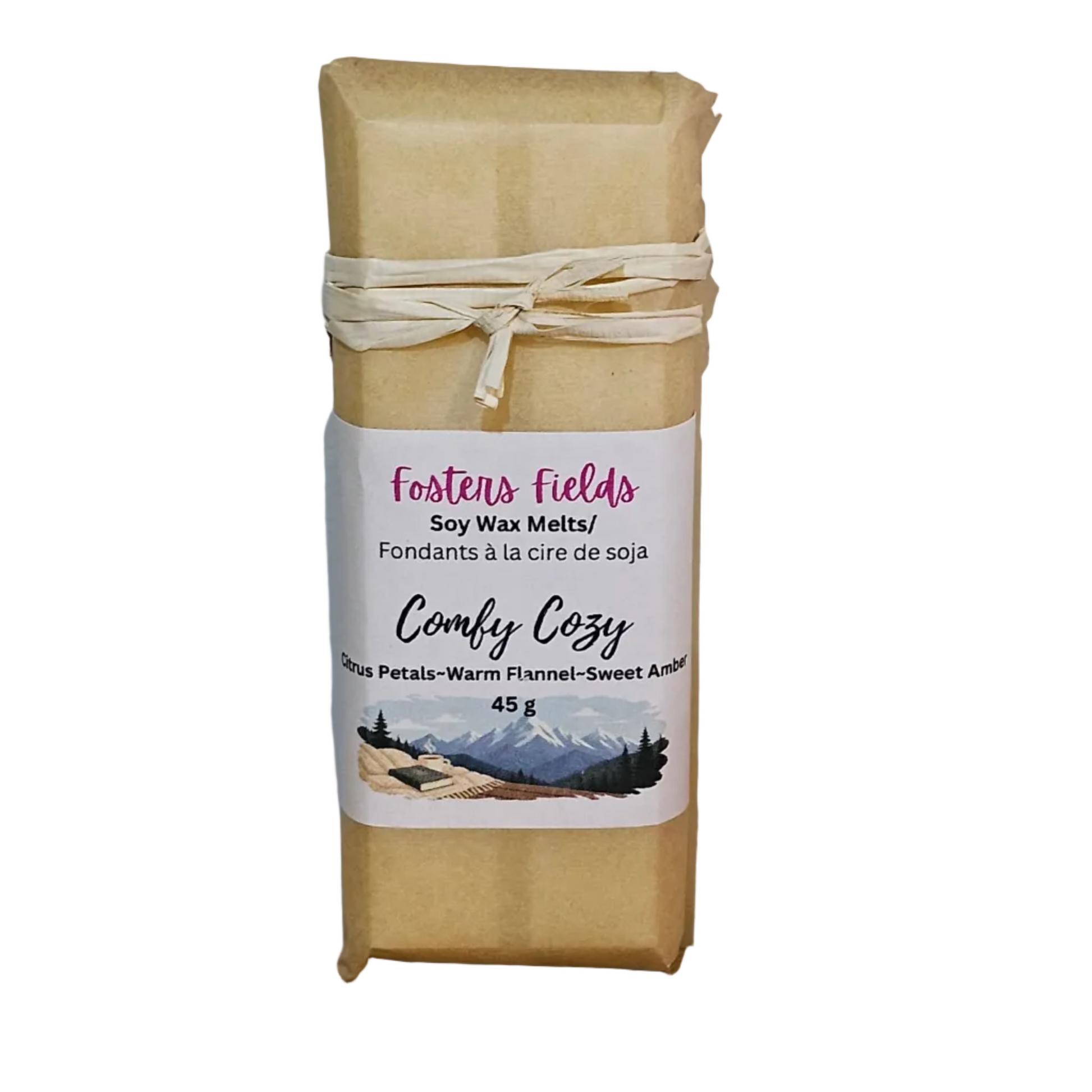 A wrapped bar of Foster's Fields soy wax melts, labeled 'Comfy Cozy,' tied with a cream ribbon and standing on a wooden surface against a plain wall.